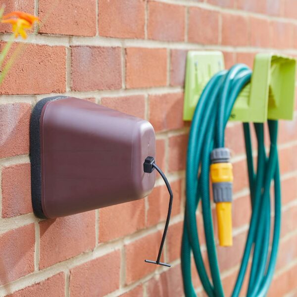 A burgundy Winter Protection Anti-Freeze Tap Cover mounted on a brick wall.
